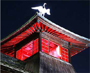 Светящаяся ночью красным башня синрокаку с фигурой белой цапли